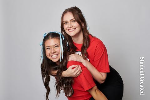 Image of a student photoshoot of two female models wearing "think 1 and thing 2" red t-shirts. They have ribbons in their hair and one model is on the back of the other model. They are both smiling and having fun