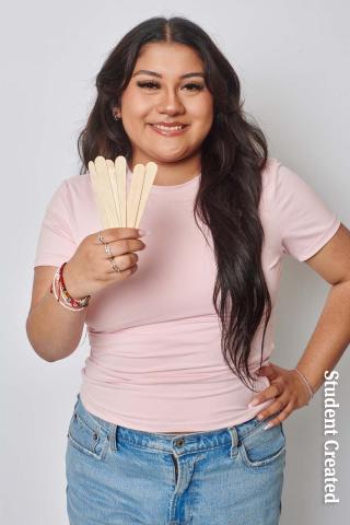 Image of a student photoshoot with a female model holding waxing sticks. Here hair is long and brown and her makeup is done. 