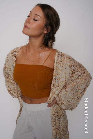 Image of a young woman student model posing with her eyes closed and wearing a copper colored shirt and ivory linen pants. Here hair is styled with braids and pulled back.